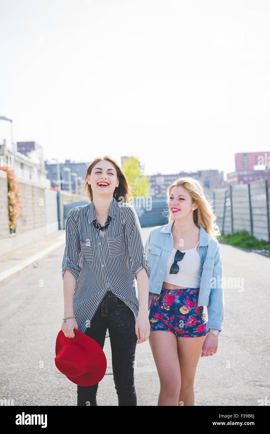 Knie-Abbildung von zwei schöne Blonde und Brünette Freunde zu Fuß durch die Stadt Lächeln, Spaß - Freundschaft, Emanzipation Konzept - mit Blick auf Links, die andere mit Blick auf rechts Stockfoto