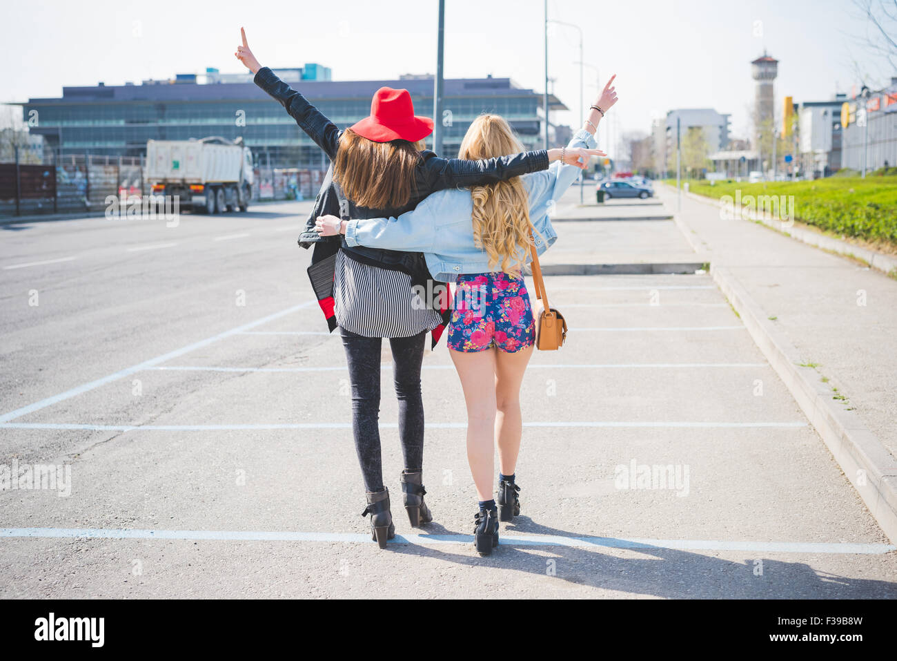 Zwei schöne blonde und Brünette Freunde Spaziergang durch die Stadt umarmt, Hände oben in der Luft, Spaß - Freundschaft, Emanzipation, Glück Konzept - von hinten anzeigen Stockfoto
