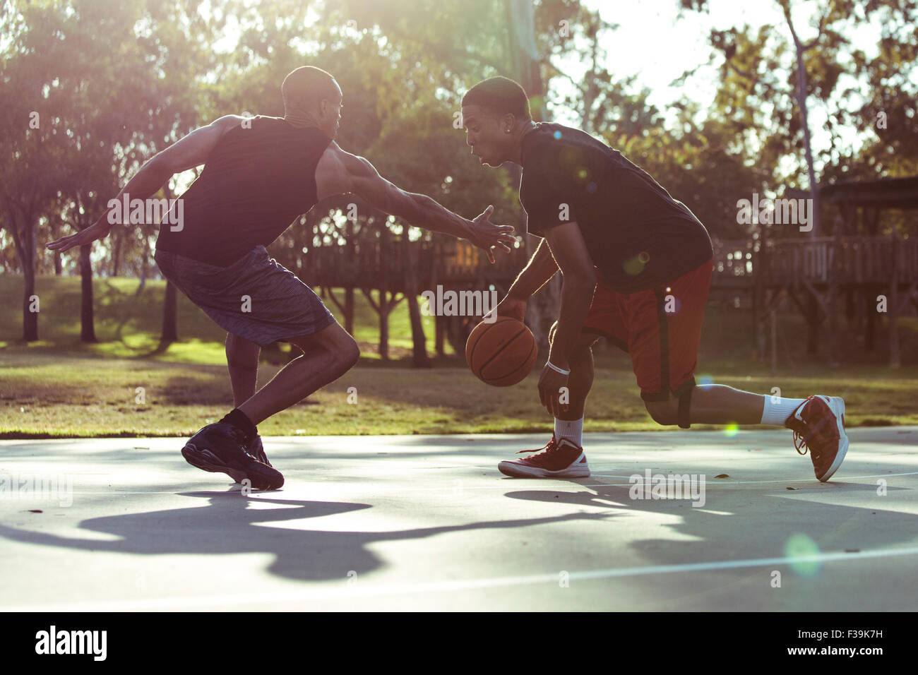 Zwei junge Männer spielen Basketball im Park bei Sonnenuntergang Stockfoto