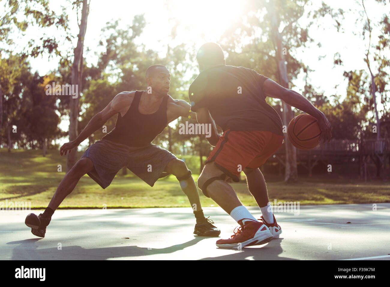 Zwei junge Männer spielen Basketball im Park bei Sonnenuntergang Stockfoto