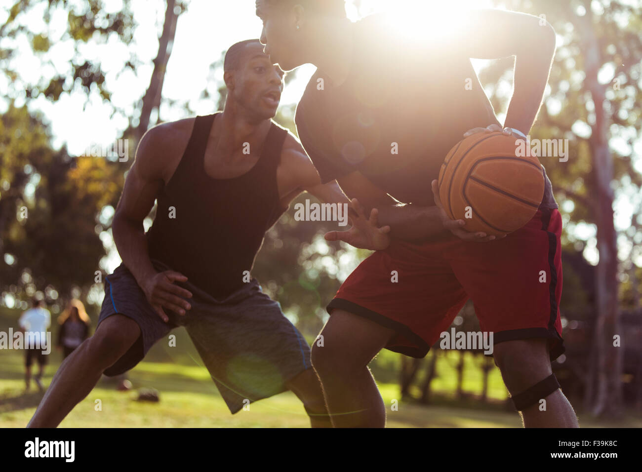 Zwei junge Männer spielen Basketball im Park bei Sonnenuntergang Stockfoto