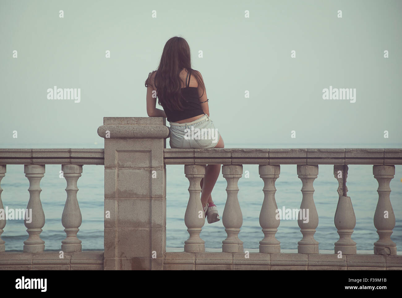 Rückansicht der ein junges Mädchen sitzt auf einer Mauer mit Blick aufs Meer Stockfoto