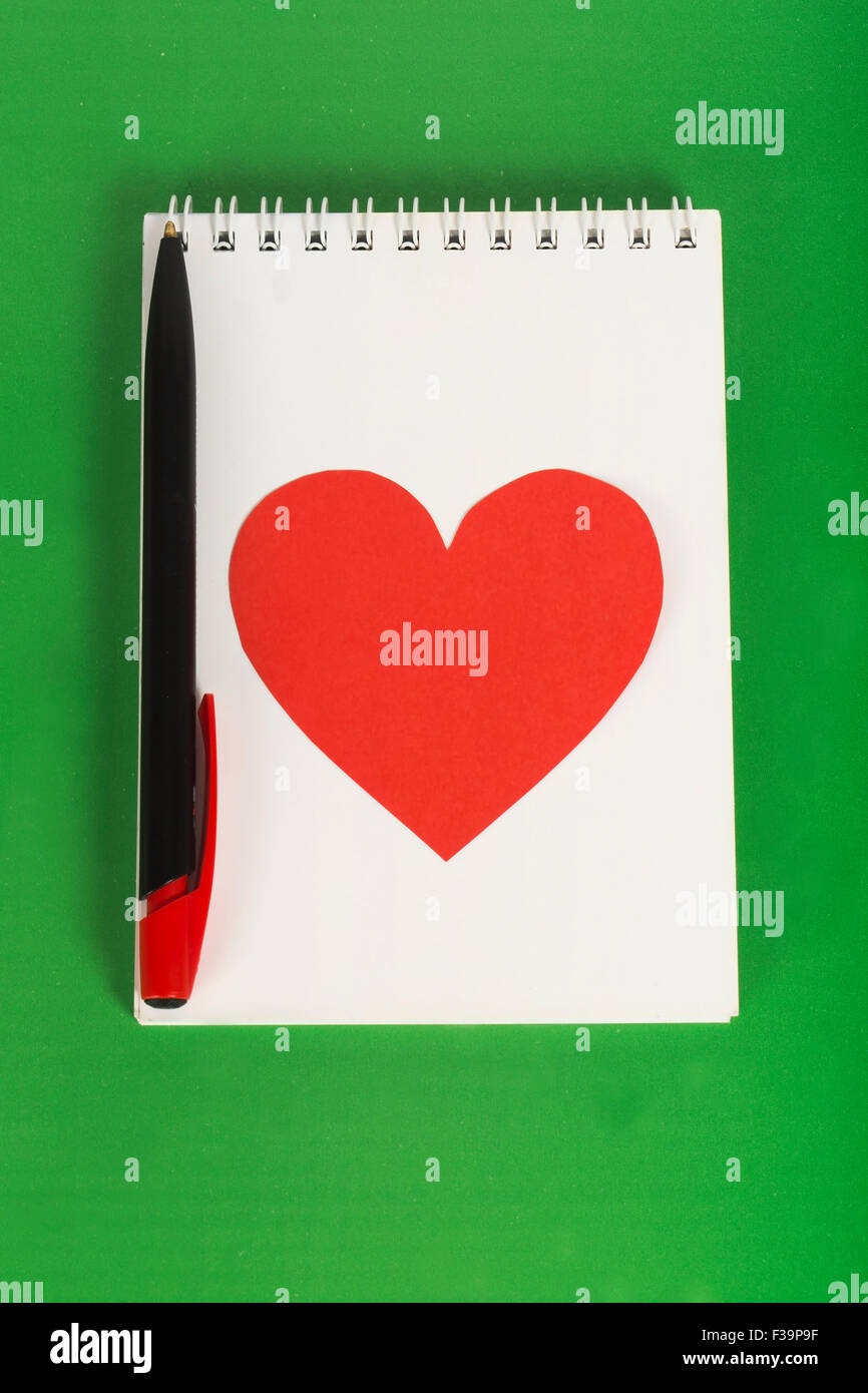 Rotes Herz mit schwarzem Stift auf weißem Notebook auf grünem Hintergrund Stockfoto