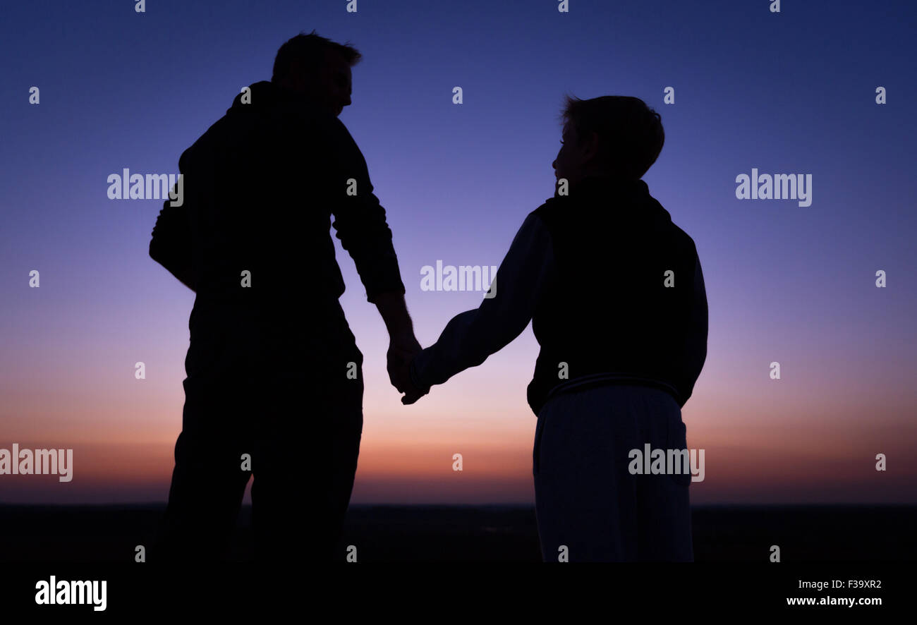 Förderung und Erziehung Konzept Foto von Vater und Sohn in der Silhouette, die Hand in Hand, den Sonnenuntergang beobachten Stockfoto