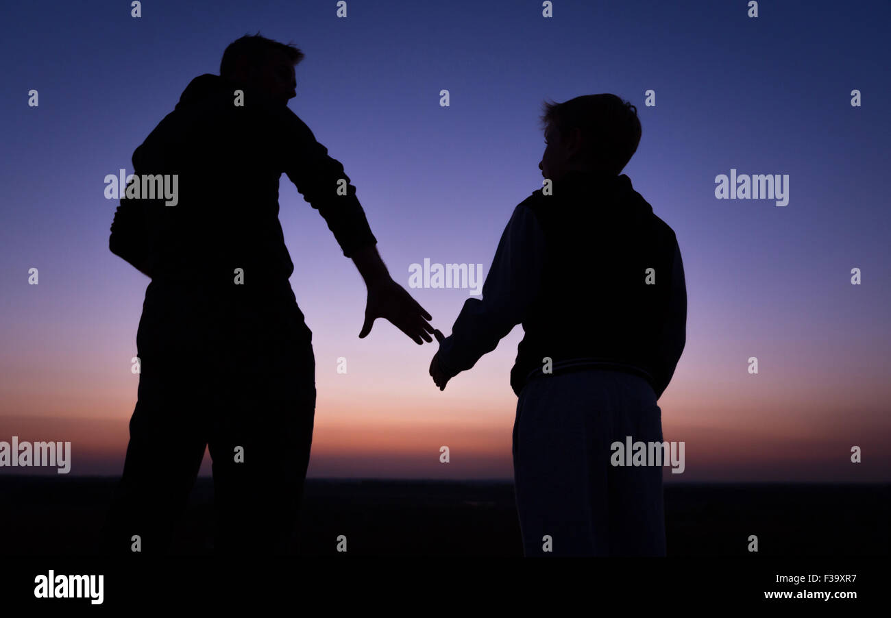 Förderung und Erziehung Konzept Foto von Vater und Sohn in der Silhouette, die Hand in Hand, den Sonnenuntergang beobachten Stockfoto