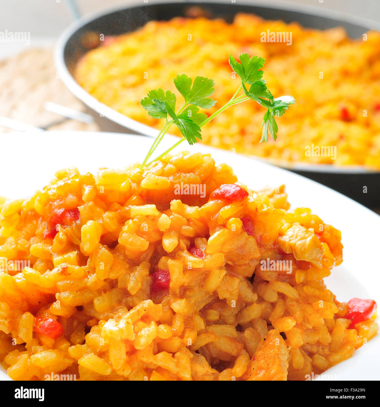 Nahaufnahme von einem Teller mit spanischen Hähnchen Paella und eine Paella-Pfanne mit mehr Hähnchen Paella im Hintergrund Stockfoto