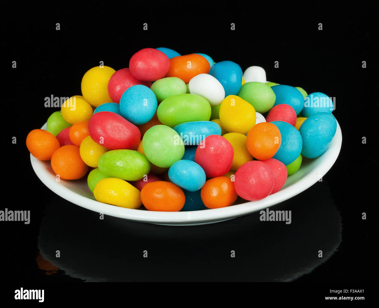 bunte Bonbons in weiße Untertasse auf schwarzem Hintergrund isoliert Stockfoto