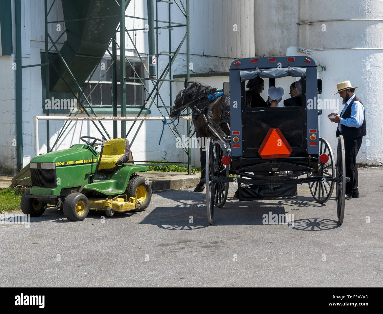 Amische Pferd und quadratischen Wagen parkte neben einem John Deere LX188 Fahrt auf Rasenmäher Stockfoto