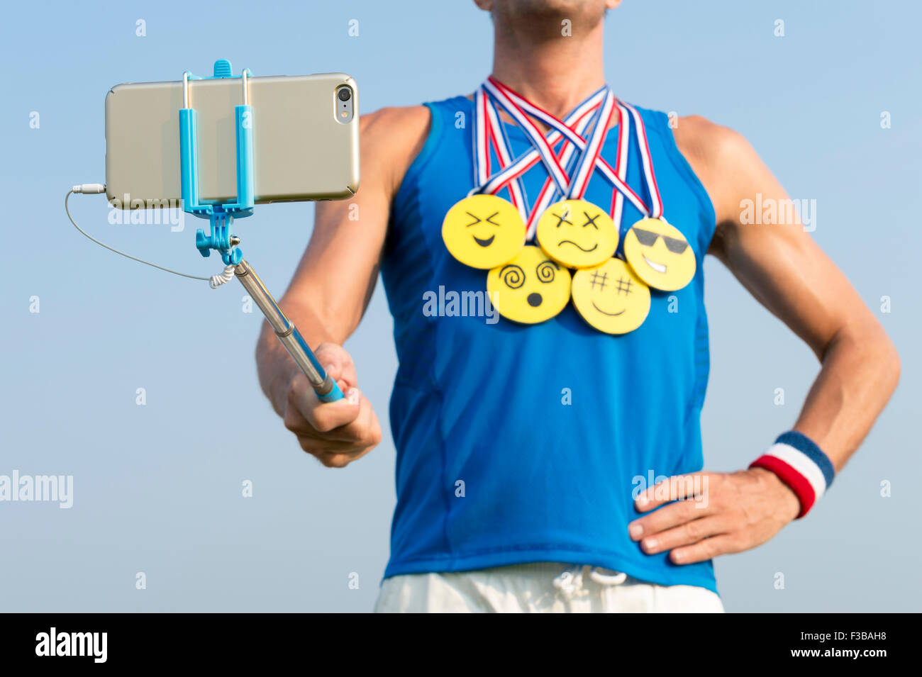 Sportler nehmen Selfie tragen Goldmedaillen mit hellen gelben Emoji Gesichter mit Smartphone auf Selfie stick Stockfoto