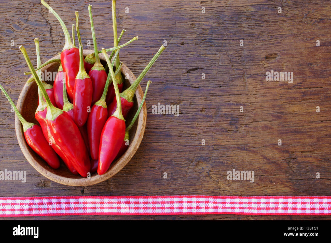 Red Chili-Pfeffer-Hülsen in einer Holzschale auf einem rustikalen Holztisch mit Webband mit textfreiraum als Menükarte Stockfoto