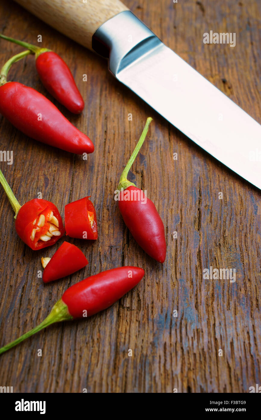Rot scharf geschnittene Chilischoten und ein Küchenmesser auf alten rustikalen Holztisch Stockfoto
