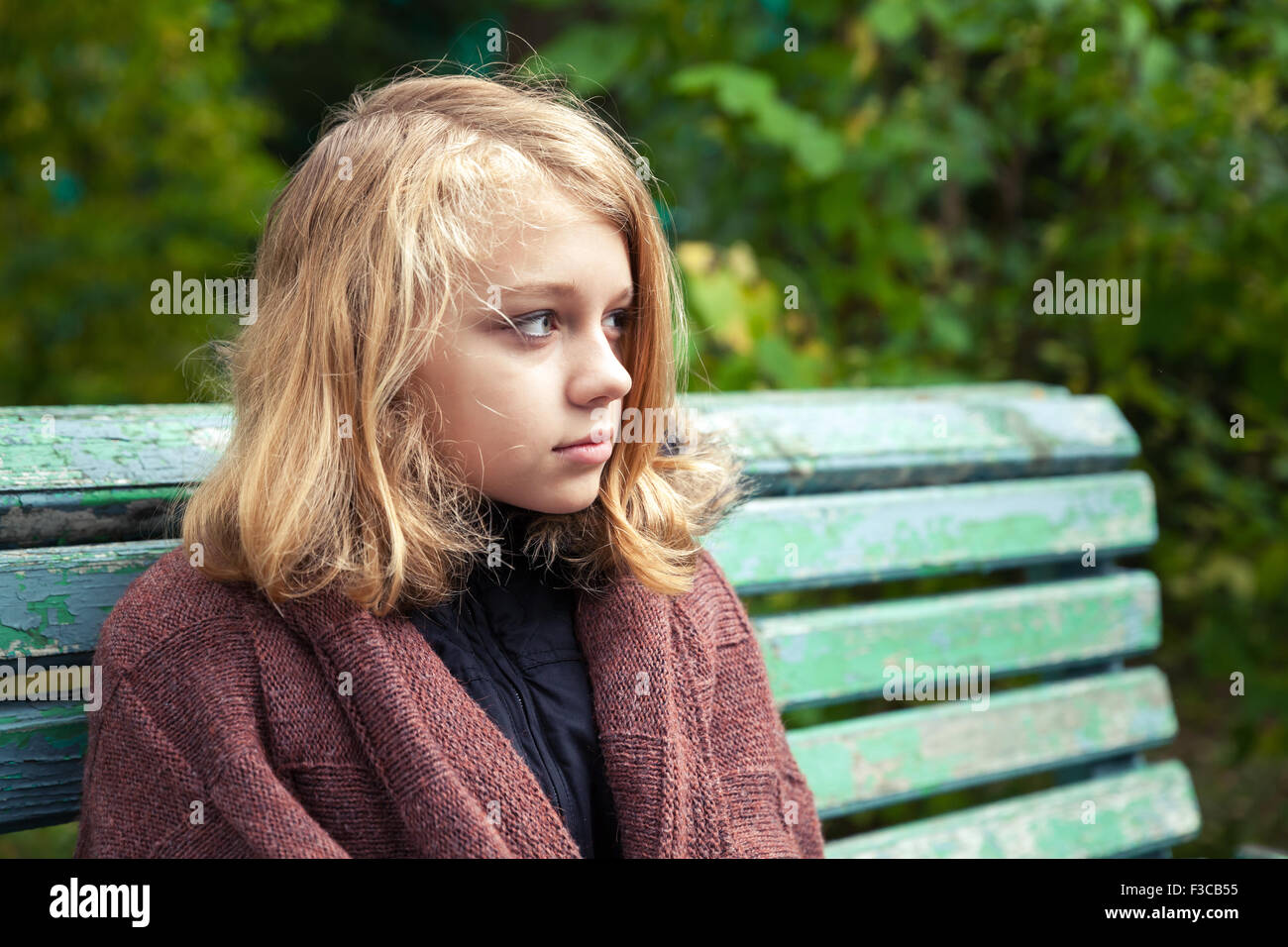 Schöne kaukasischen blonde Teenager-Mädchen in wollenen Plaid sitzt auf alten grünen Bank im Herbst Park Stockfoto