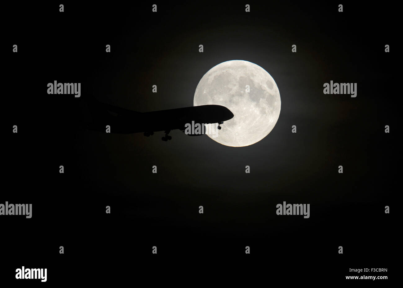 Silhouette eines Flugzeuges über den Weg einer Vollmondnacht, wie das Flugzeug ins Land am Flughafen Manchester, England steigt. Stockfoto