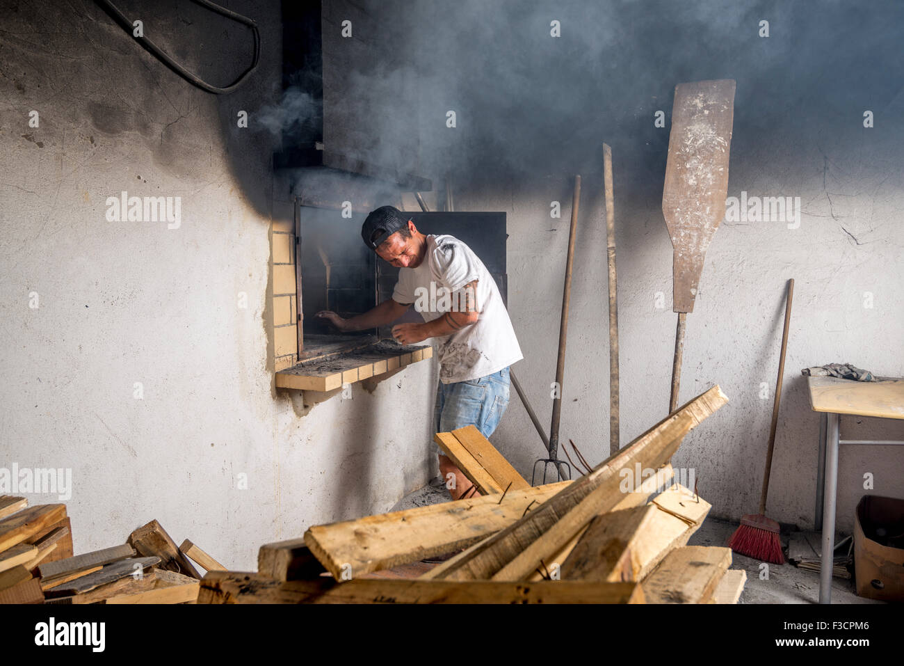 Junge Bäcker Feuer im Steinofen, verursacht viel Rauch. Stockfoto