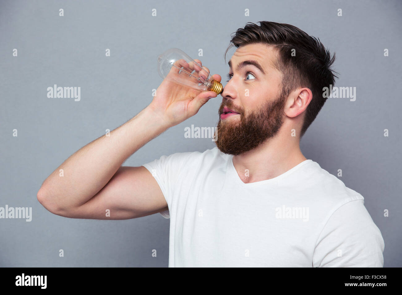 Porträt von einem lustigen Mann wegsehen durch Glühbirne über grauen Hintergrund Stockfoto