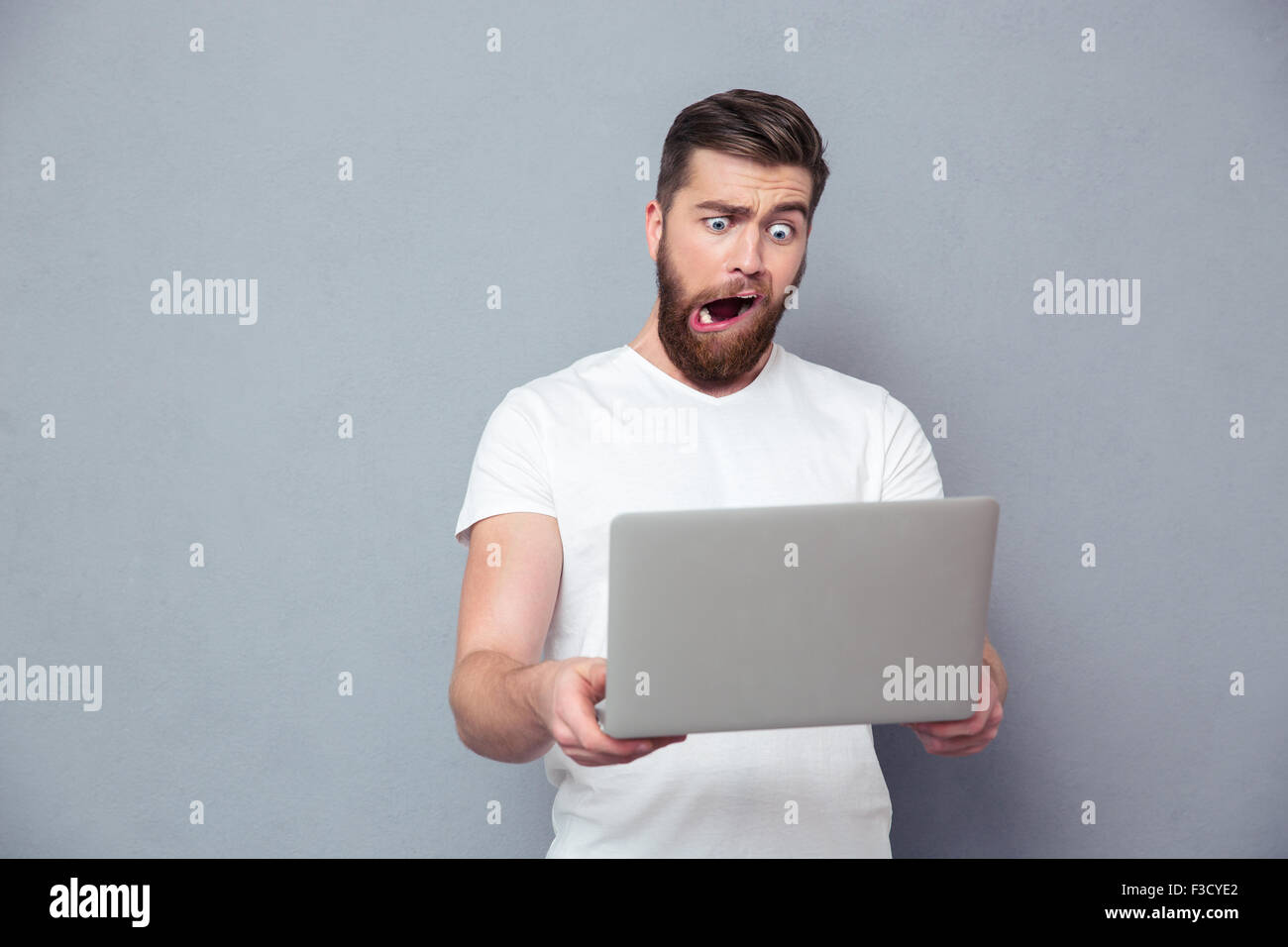 Porträt eines Mannes mit dummen Becher mit Laptop über grauen Hintergrund Stockfoto