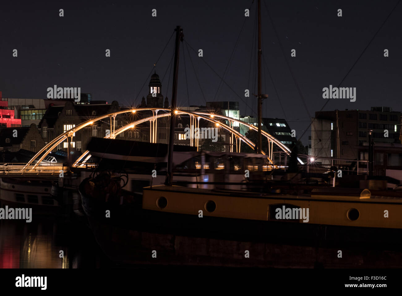 Nachtaufnahme von "Verbindingsdam" Brücke in IJhaven und Ertshaven mit Hausbooten im Vordergrund im Hafen von Amsterdam Stockfoto