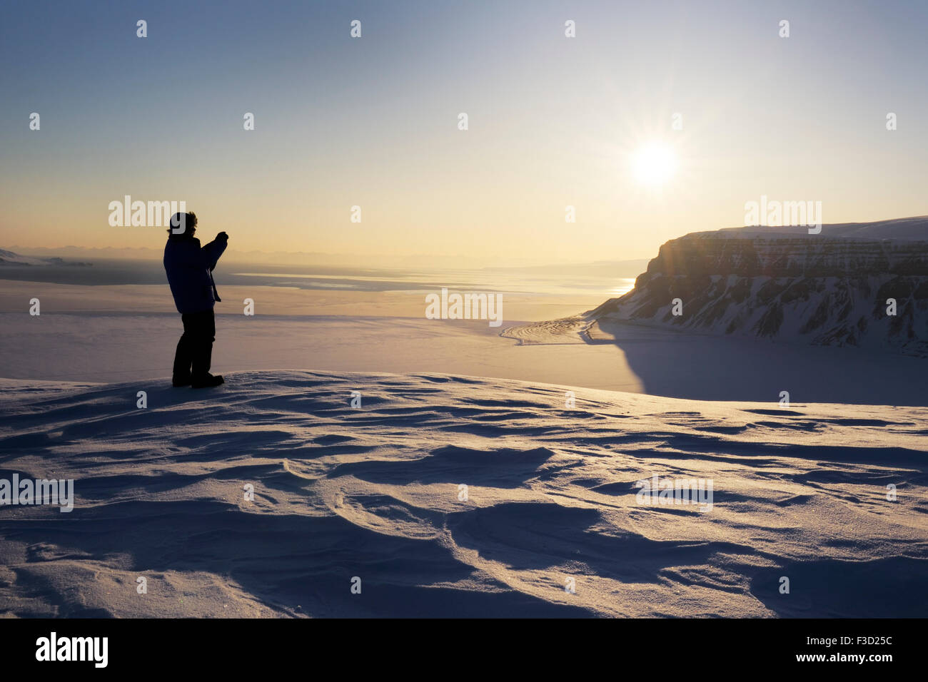 Expedition-Mitglied auf der Suche über die gefrorenen Tempelfjorden bei Sonnenuntergang, Spitzbergen (Svalbard), Norwegen. Stockfoto