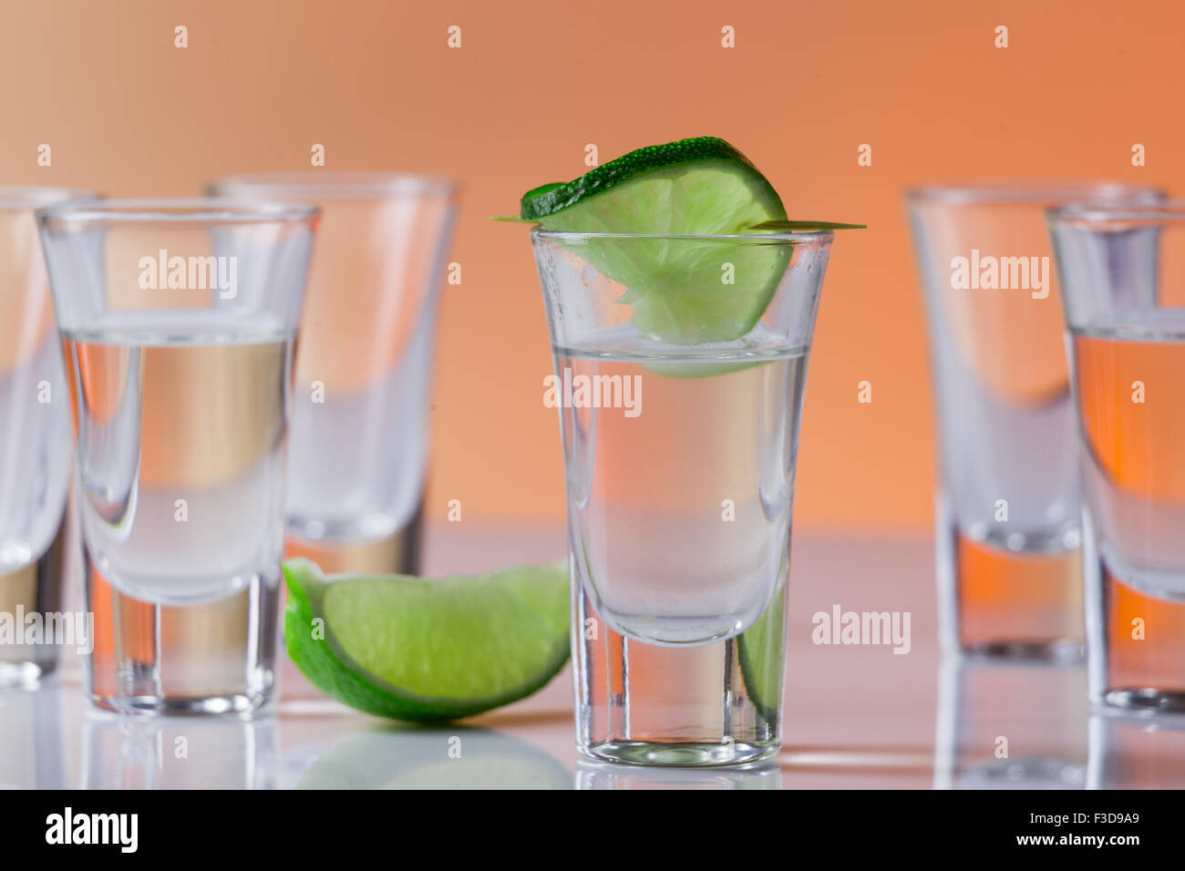 Tequila shot mit einer Scheibe Limette auf dem Glas auf orangem Hintergrund. Selektiven Fokus Stockfoto