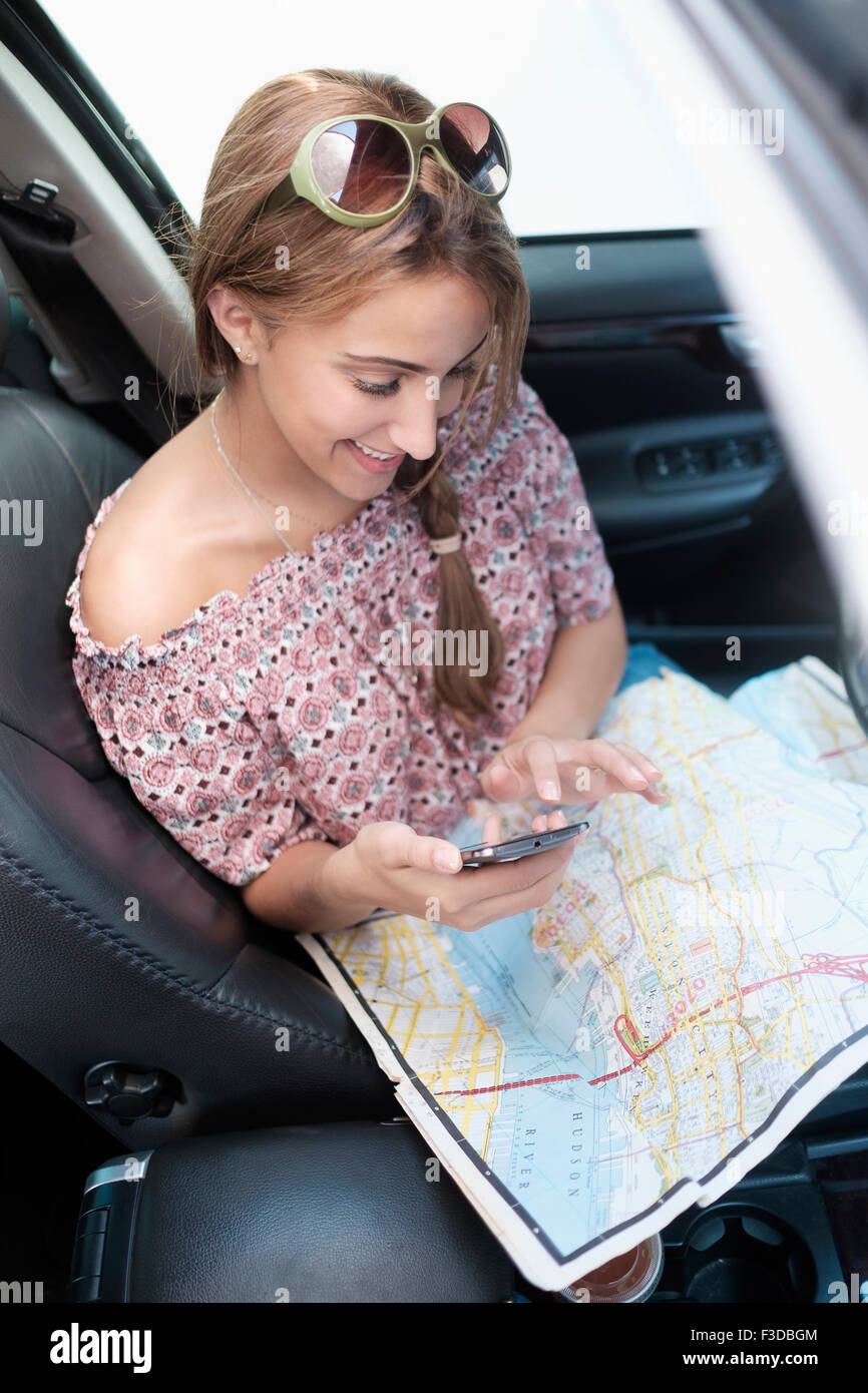 Frau überprüft Telefon im Auto mit Karte auf Schoß Stockfoto