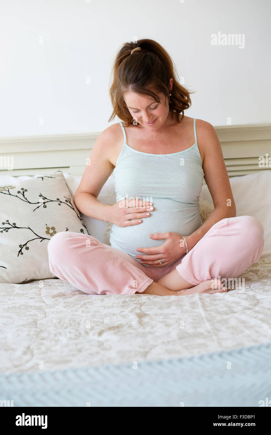 Schwangere Frau auf Bett sitzt lächelnd Stockfoto