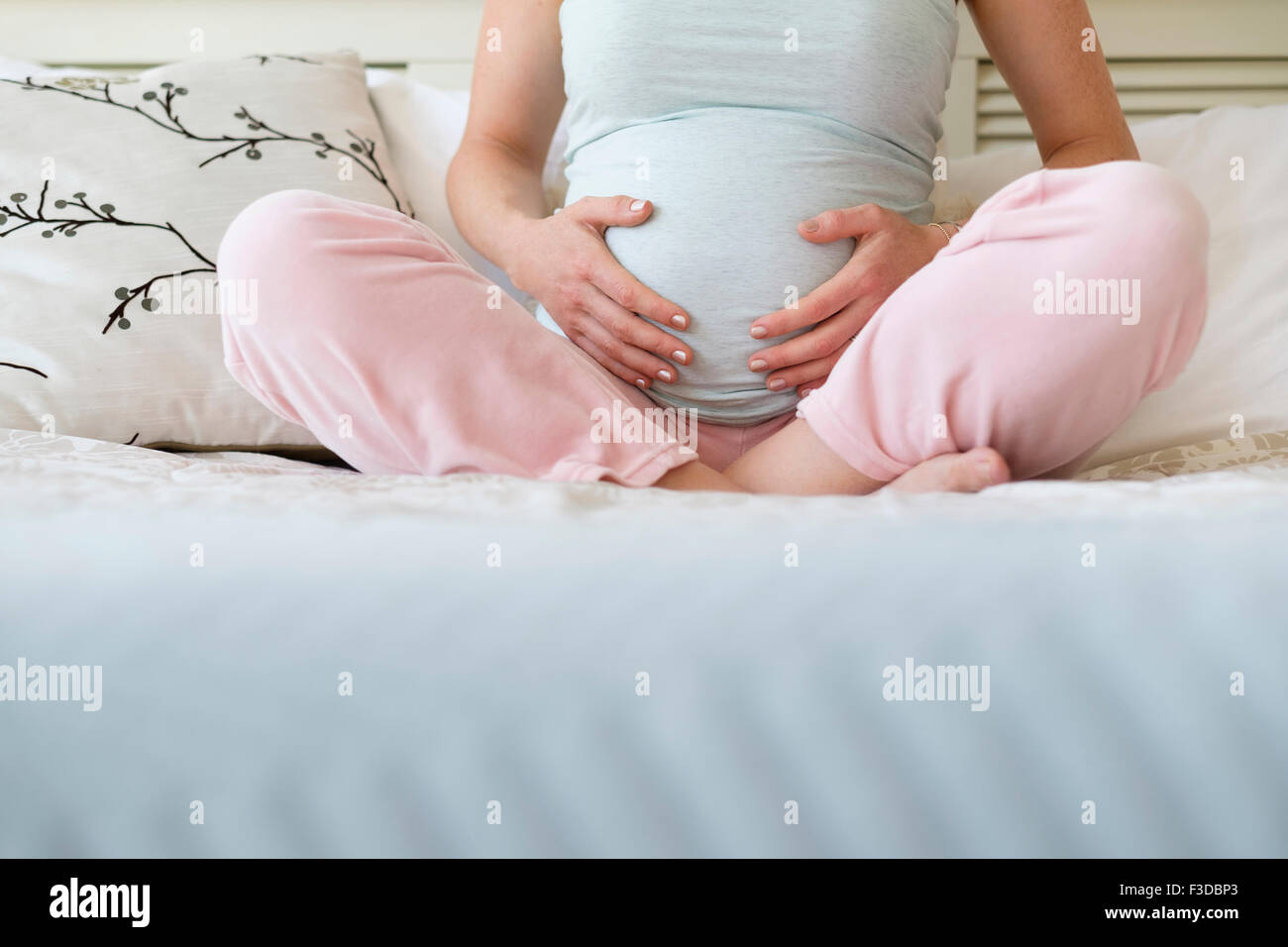 Schwangere Frau auf dem Bett sitzend Stockfoto