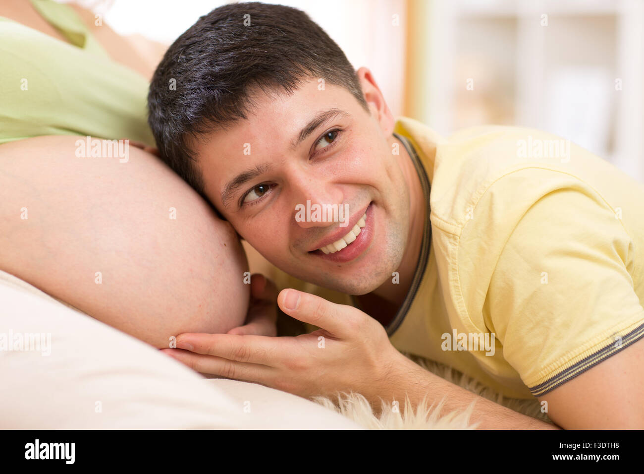 Anhören der Bauch seiner schwangeren Frau Mann Stockfoto