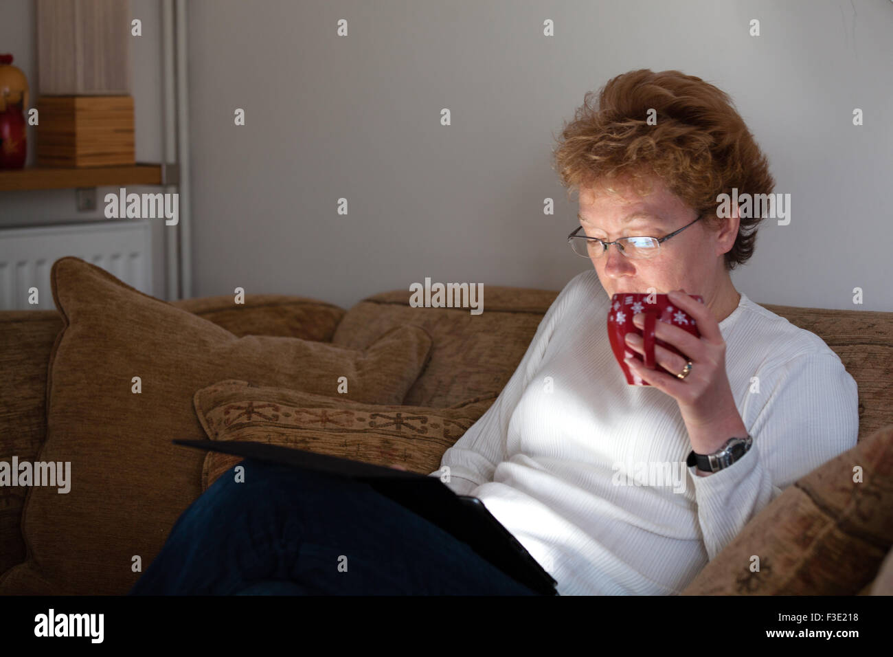 Eine Frau mittleren Alters, die zu Hause mit einer Tasse Kaffee entspannen, während das Surfen im Internet mit dem Tablet Ipad computer Stockfoto