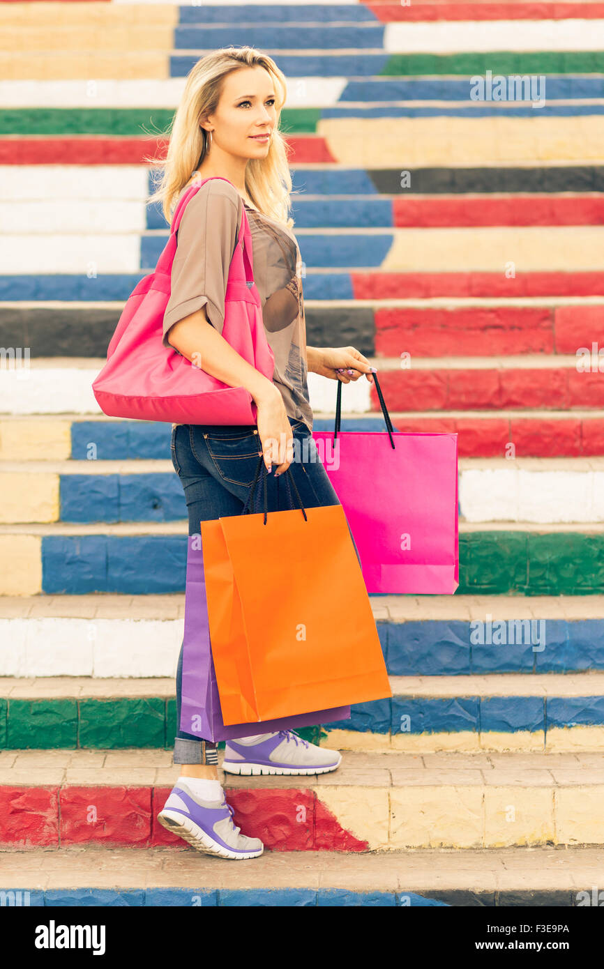 Junge schlanke blonde Frau hält Einkaufstüten steht auf der Treppe und auf der Suche zur Seite Stockfoto