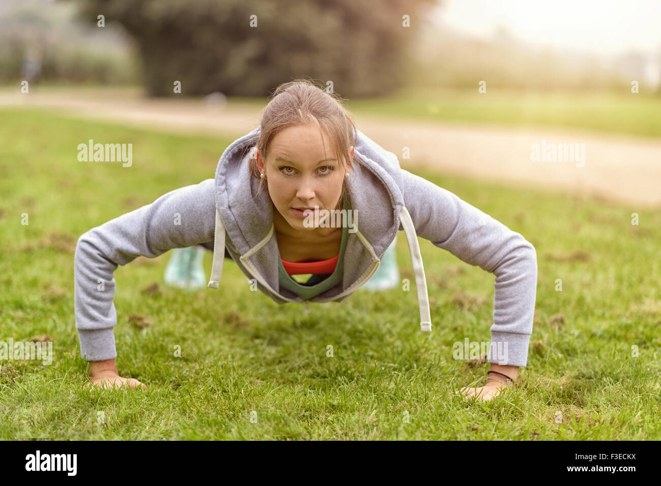 Sportliche junge Frau lächelt in die Kamera dabei Push-Up-Übung im Park. Stockfoto