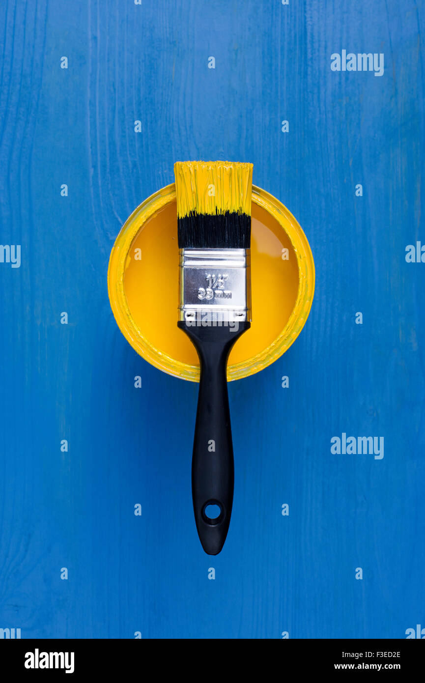Topf mit gelber Farbe und Pinsel auf einem blauen Hintergrund aus Holz Stockfoto