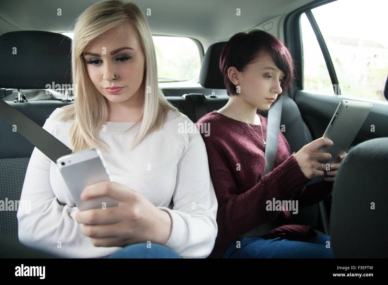 Zwei Teen Schwestern auf dem Rücksitz eines Autos halten ein Ipad Tablet und Handy. Stockfoto