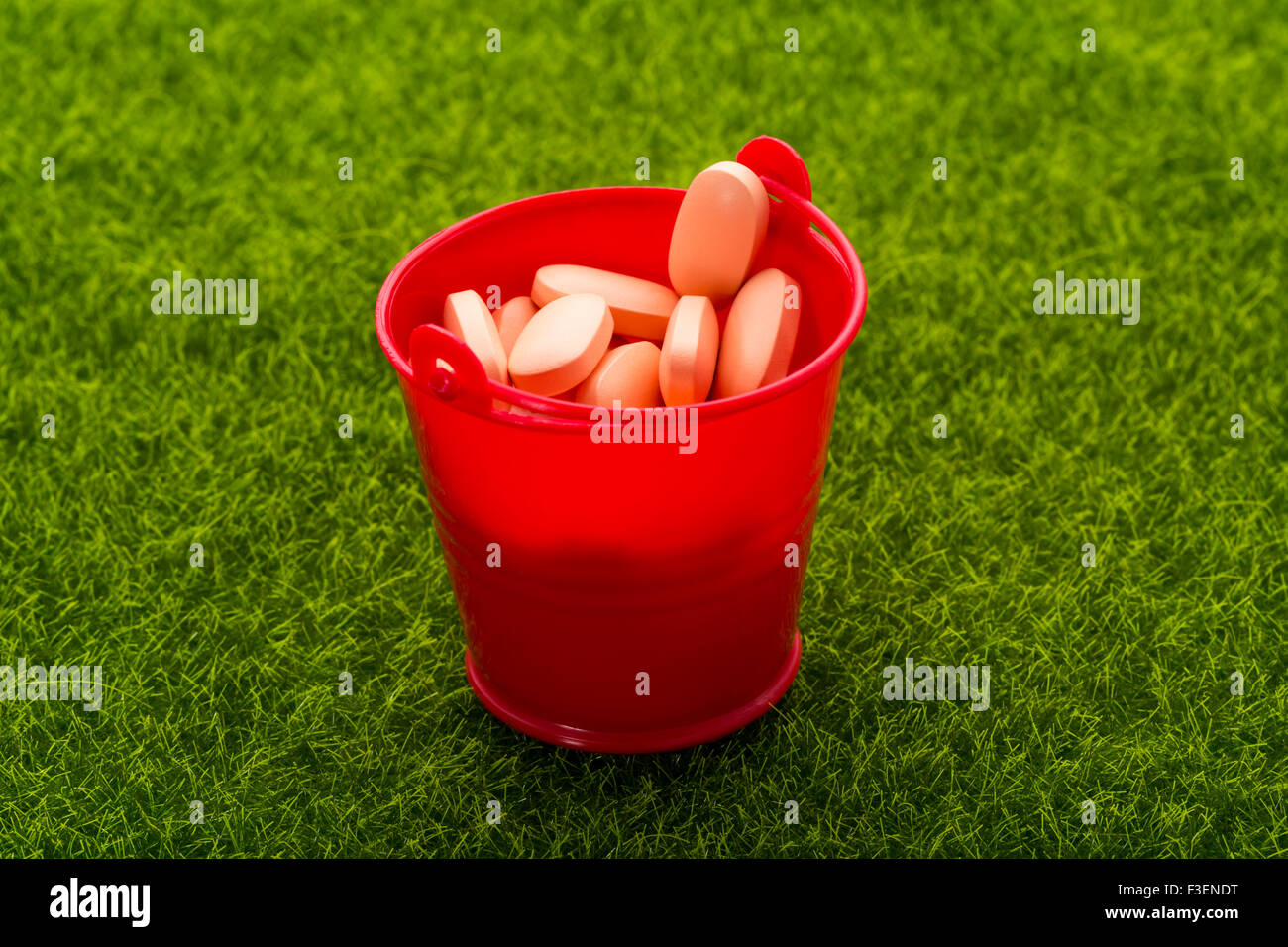 Roten Eimer voll mit orange Pillen stehen auf dem grünen Rasen. Nahaufnahme Stockfoto