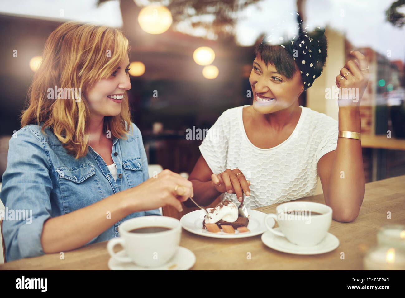 Zwei hübsche junge Frau genießen Kaffee und Kuchen zusammen in einem Kaffeehaus sitzen an einem Tisch lachten und plauderten mit happy Stockfoto