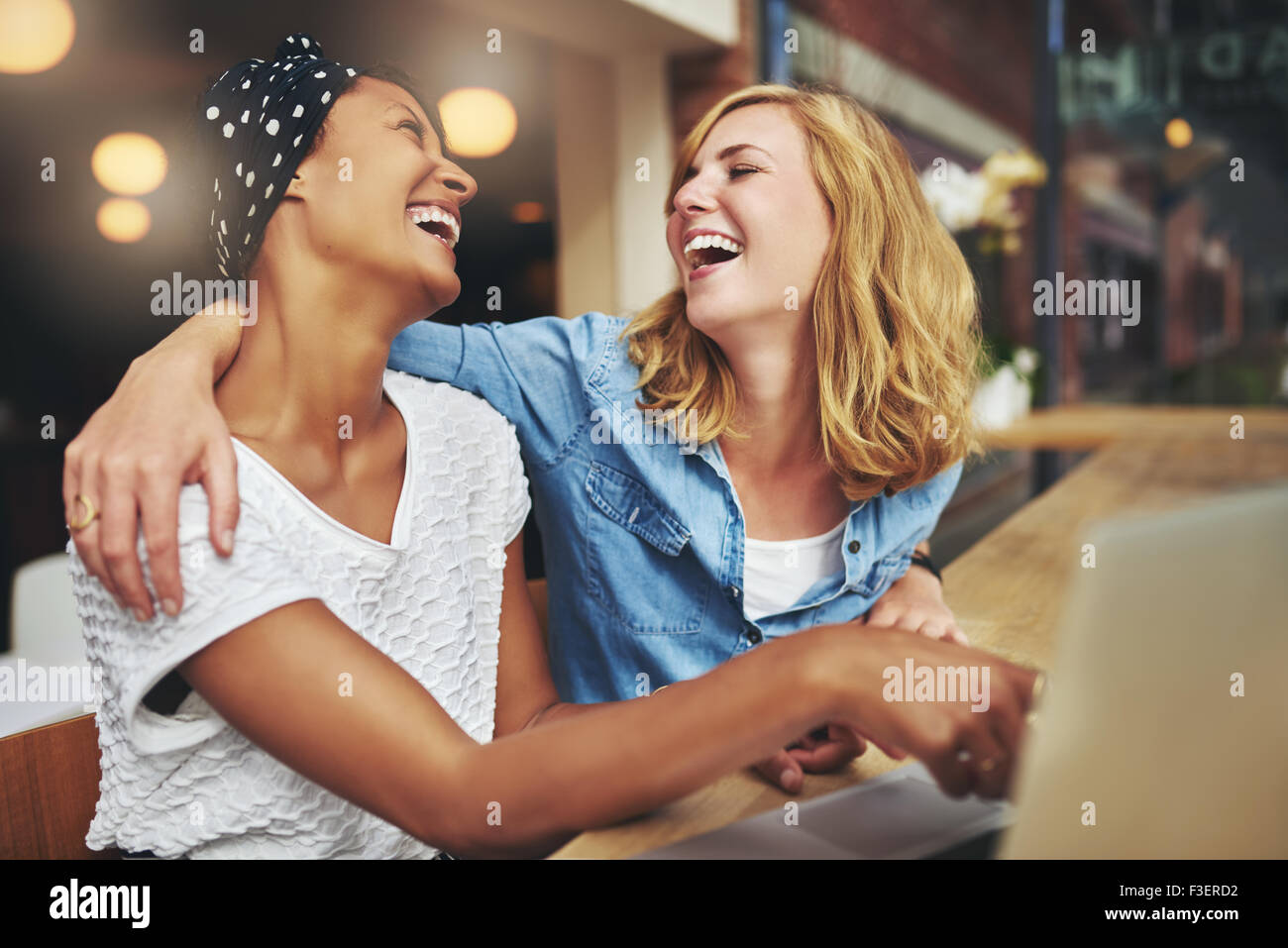 Zwei liebevolle multirassische Freundinnen umarmen und lachen, als sie auf einem Laptop-Computer-Bildschirm zeigen, dass sie teilen Stockfoto