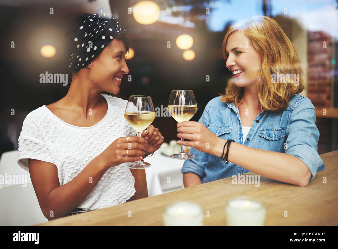Hübsche junge Frauen Toasten einander mit Gläser Weißwein, wie sie sich in ein Pub für einen entspannten Plausch treffen Stockfoto