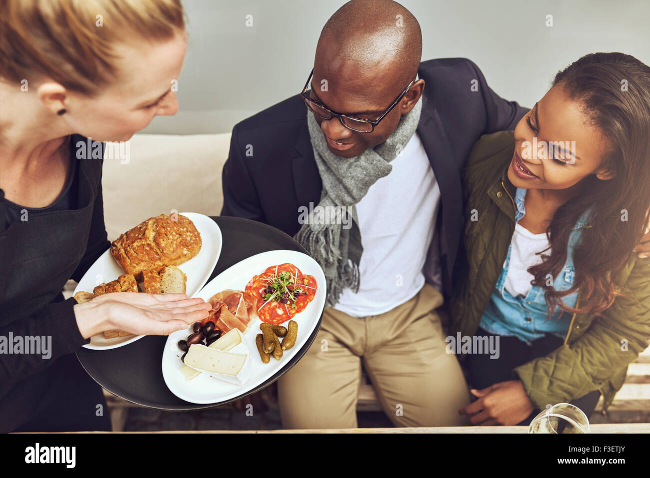 Kellnerin mit vergoldeten Küche für junge afrikanische amerikanische Kunden in einem Restaurant, erhöhte Ansicht zeigt das Essen auf den Tellern Stockfoto