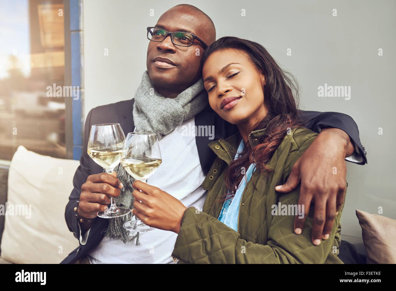 Glückseligen romantisch junge afrikanische zu zweit entspannen im jeweils anderen Arme und genießen Sie einen Schluck Weißwein auf einem Tisch im restaurant Stockfoto