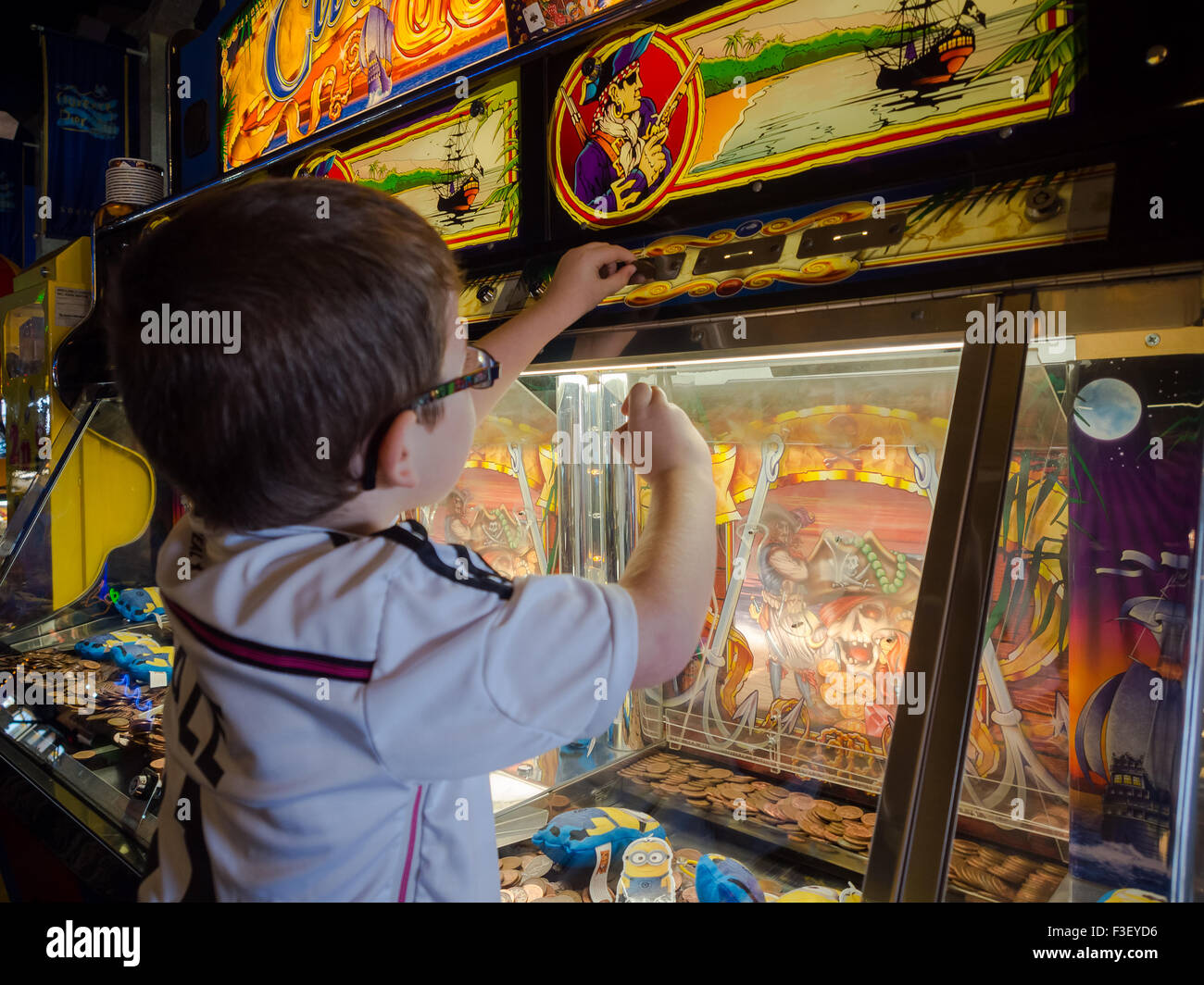 Ein sehr kleiner Junge spielt auf einem Spielautomaten in einer Spielhalle penny Stockfoto