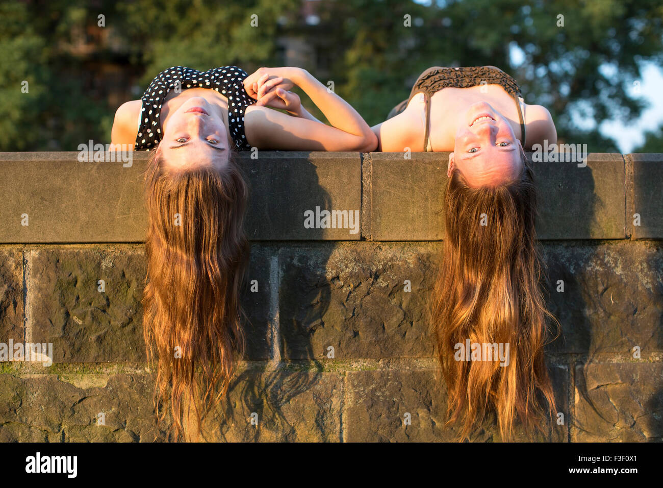 Zwei junge Mädchen liegend auf einem Stein Tafel mit langen Haaren hängen nach unten. Schönes weiches Licht bei Sonnenuntergang. Stockfoto