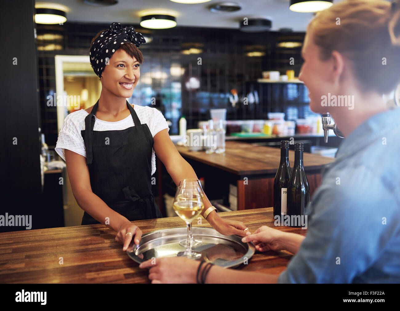 Fröhliche Kellnerin serviert Gläser Wein auf einem silbernen Tablett zu einer Kundin in der Kneipe. Stockfoto