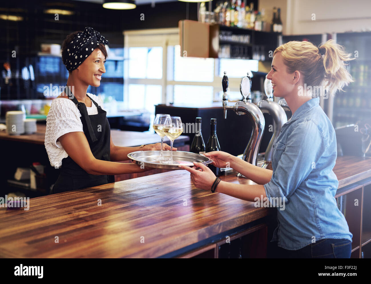 Lächelnde Kellnerin geben Gläser Wein auf einem Tablett zu einer Kundin an der Bar zu begegnen. Stockfoto
