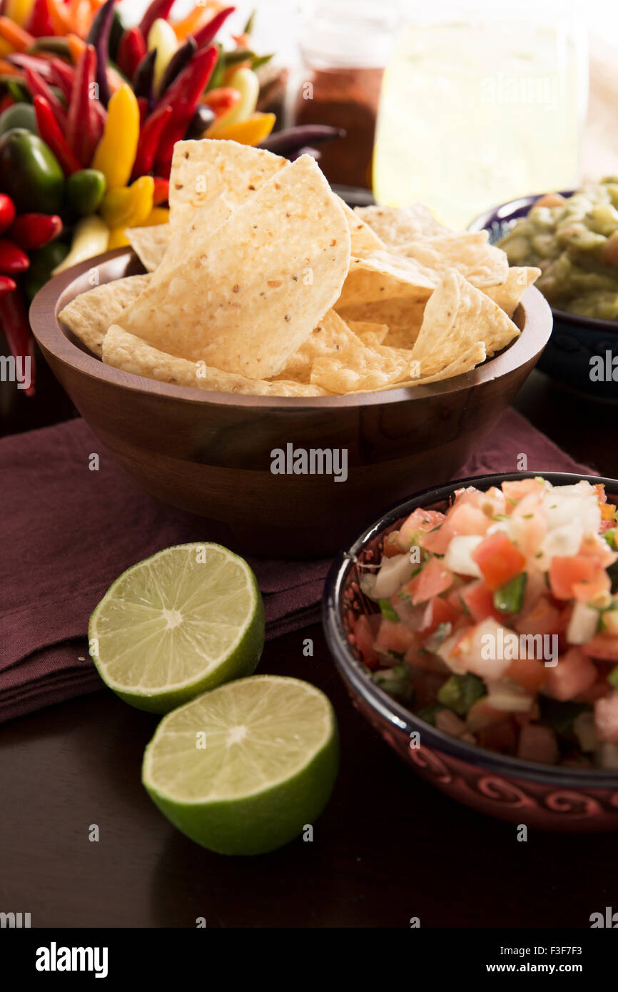 Frische Tortillachips mit Pico de Gallo und frischen Limetten in Vordergrund, Guacamole und Margarita im Hintergrund. Stockfoto