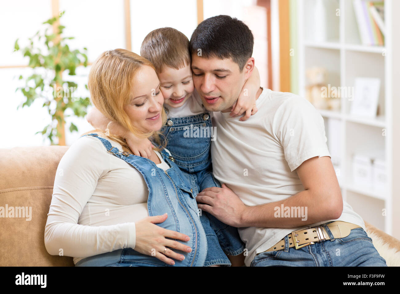 Glückliche Familie erwartet Baby. Schwangere Frau mit Mann und Ihrem kleinen Sohn zusammen zu Hause auf dem Sofa sitzen Stockfoto