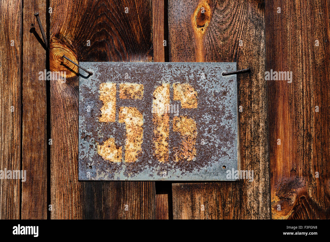 Alte rostige Platte mit Hausnummer angenagelt an einer Holzwand einer Scheune Stockfoto