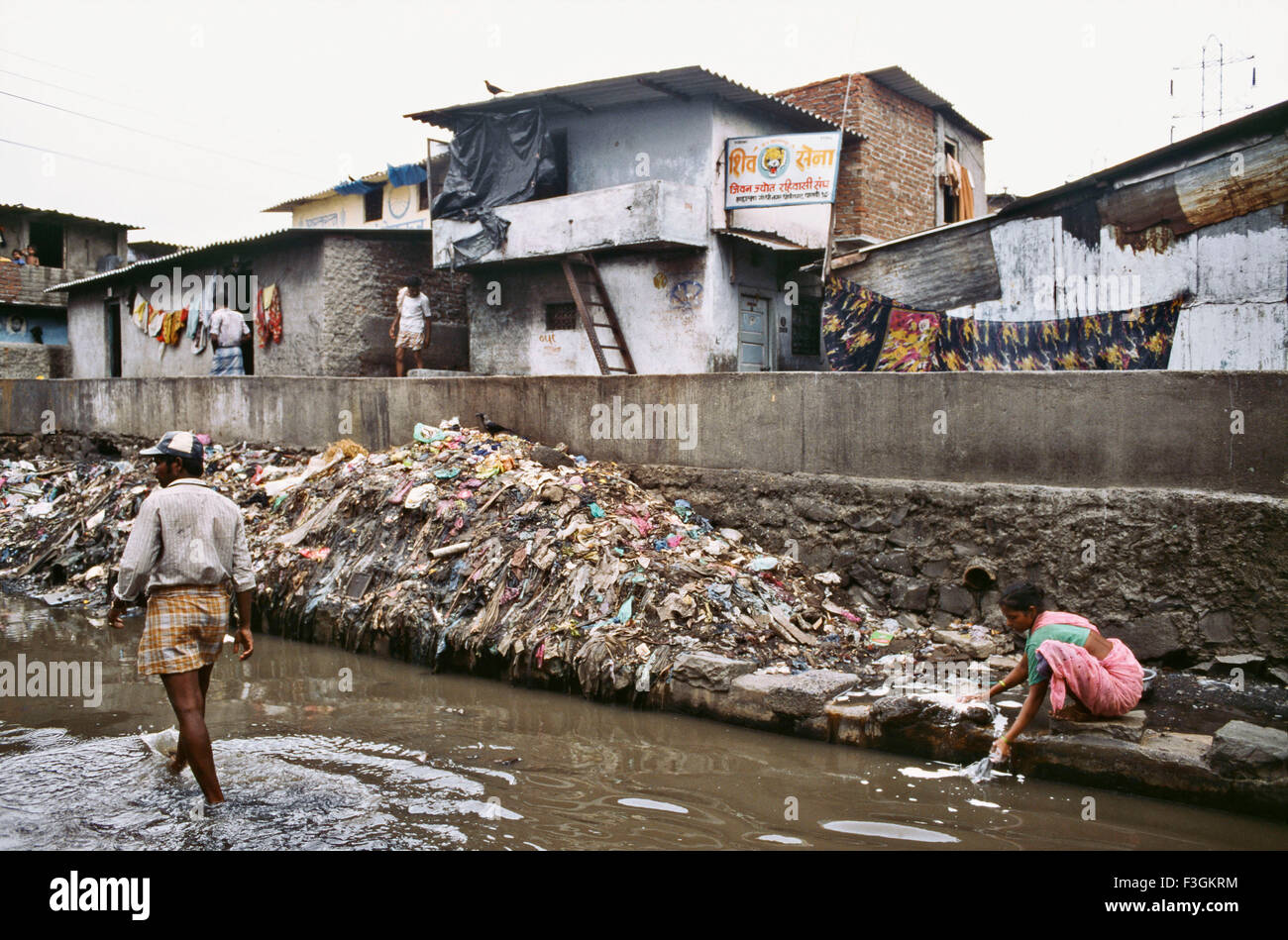 Frau, die Tuch im schmutzigen Wasser entlang eines Kanals wäscht, der mit Abfall in einem Slum in Bombay jetzt Mumbai gedumpt wird; Maharashtra; Indien; Asien Stockfoto