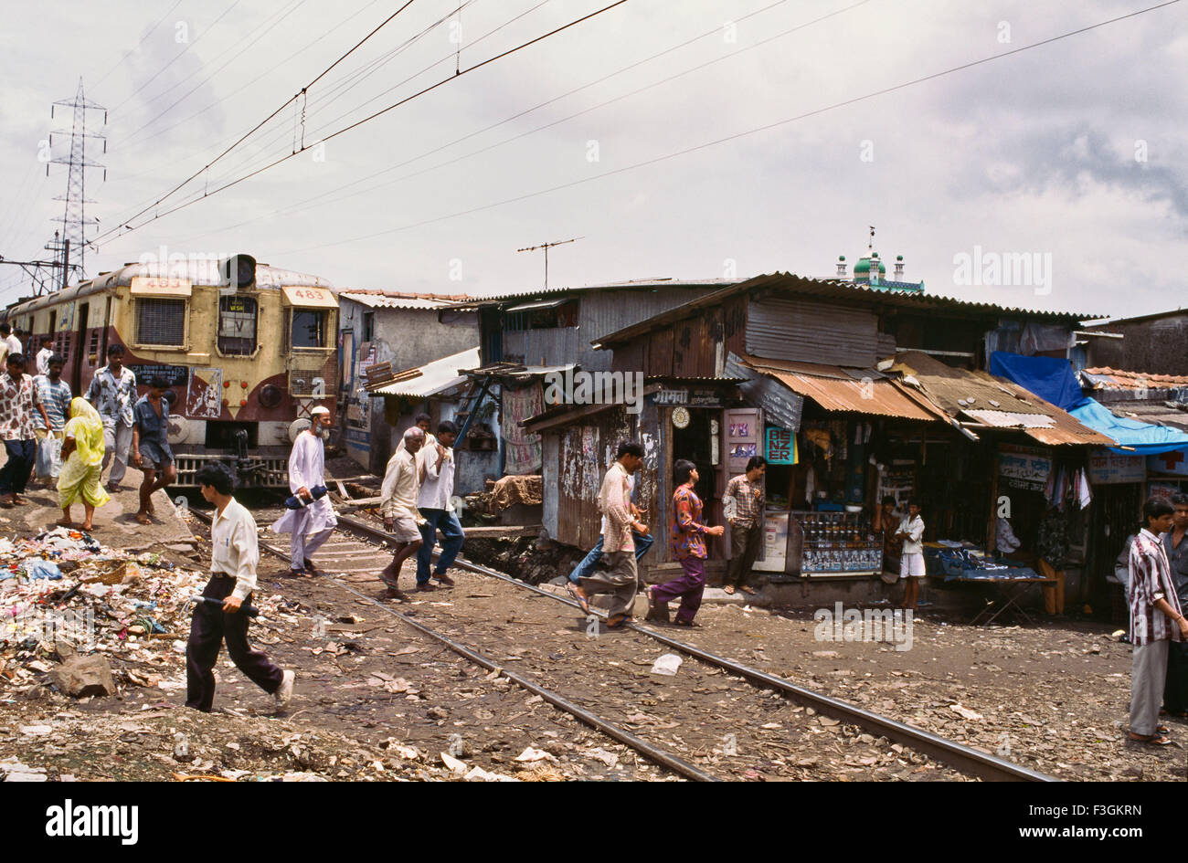 Pendler, die Überquerung der Bahnlinie, die s-Bahn dicht verläuft dehnen mit Slums entlang seiner Seite Govandi Station Mumbai Stockfoto