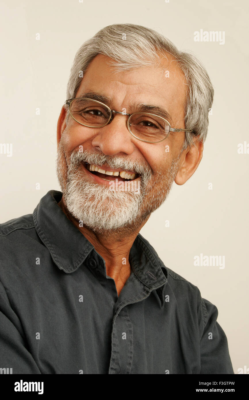 South Asian indischen alte Mann Ende der fünfziger Jahre mit grauem Haar und Bart tragen, dunkelblauen Hemd und Brille zufriedenstellend lachen Stockfoto