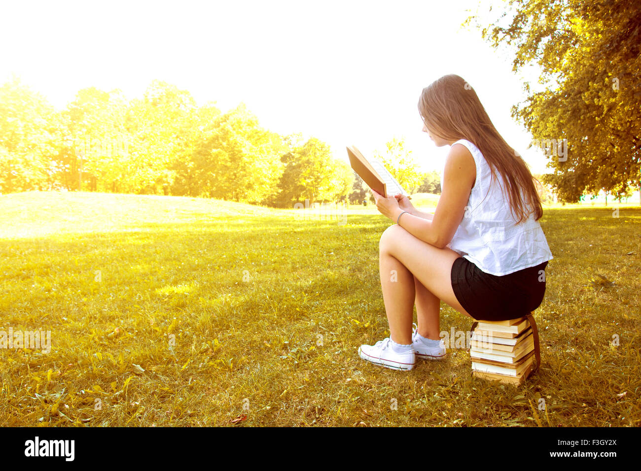 Attraktive weibliche College-Student, ein Buch lesen und sitzen auf den Bücherstapel. Bildung. Zurück zu Schule Konzeptbild. Stockfoto