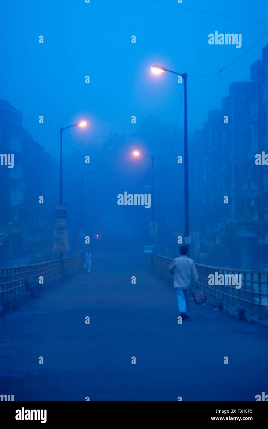 Mann zu Fuß vorbei an leuchtenden Straßenlaternen unter blauen nebligen Morgen; Mulund; Bombay Mumbai; Maharashtra; Indien Stockfoto